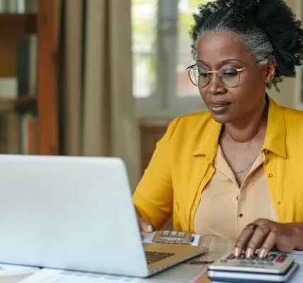 Focused-millennial-Black-business-woman-calculating-finance-money-using-calculator-laptop-computer-at-home-workplace-table-counting-budget-paying-bills-taxes-rent-mortgage-fees