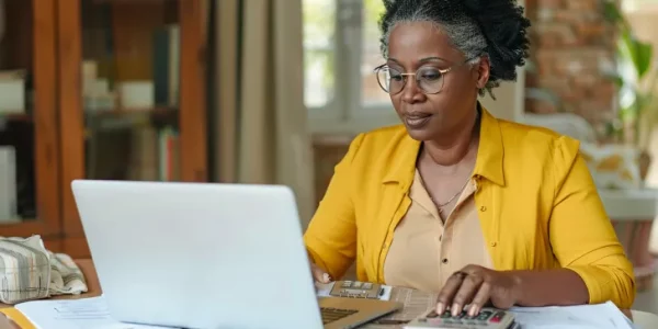 Focused-millennial-Black-business-woman-calculating-finance-money-using-calculator-laptop-computer-at-home-workplace-table-counting-budget-paying-bills-taxes-rent-mortgage-fees